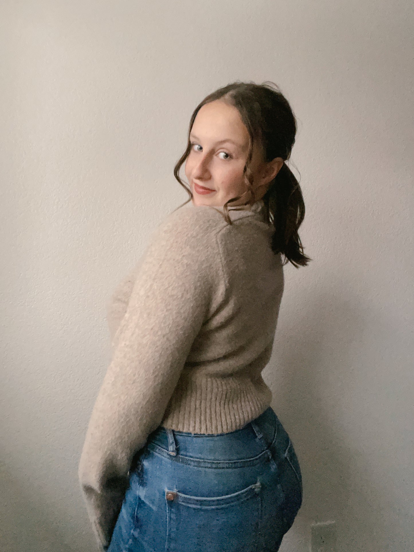 Woman wearing a beige sweater and blue jeans against a plain background Beige Knit Sweater | From the Rack | Grace Thrifts