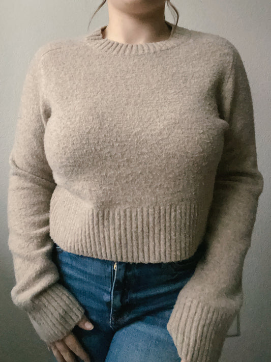 Woman wearing a beige sweater and blue jeans against a plain background Beige Knit Sweater | From the Rack | Grace Thrifts