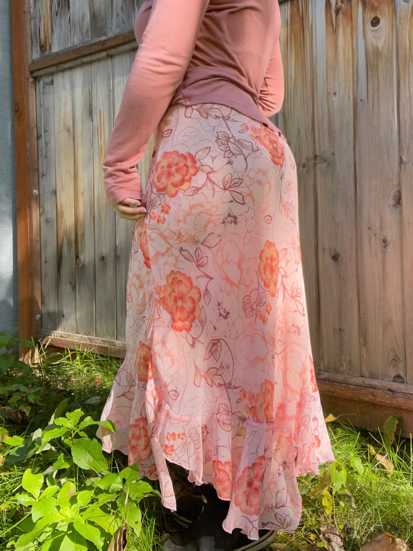 Person wearing a floral skirt with a wooden fence and greenery in the background | Grace Thrifts