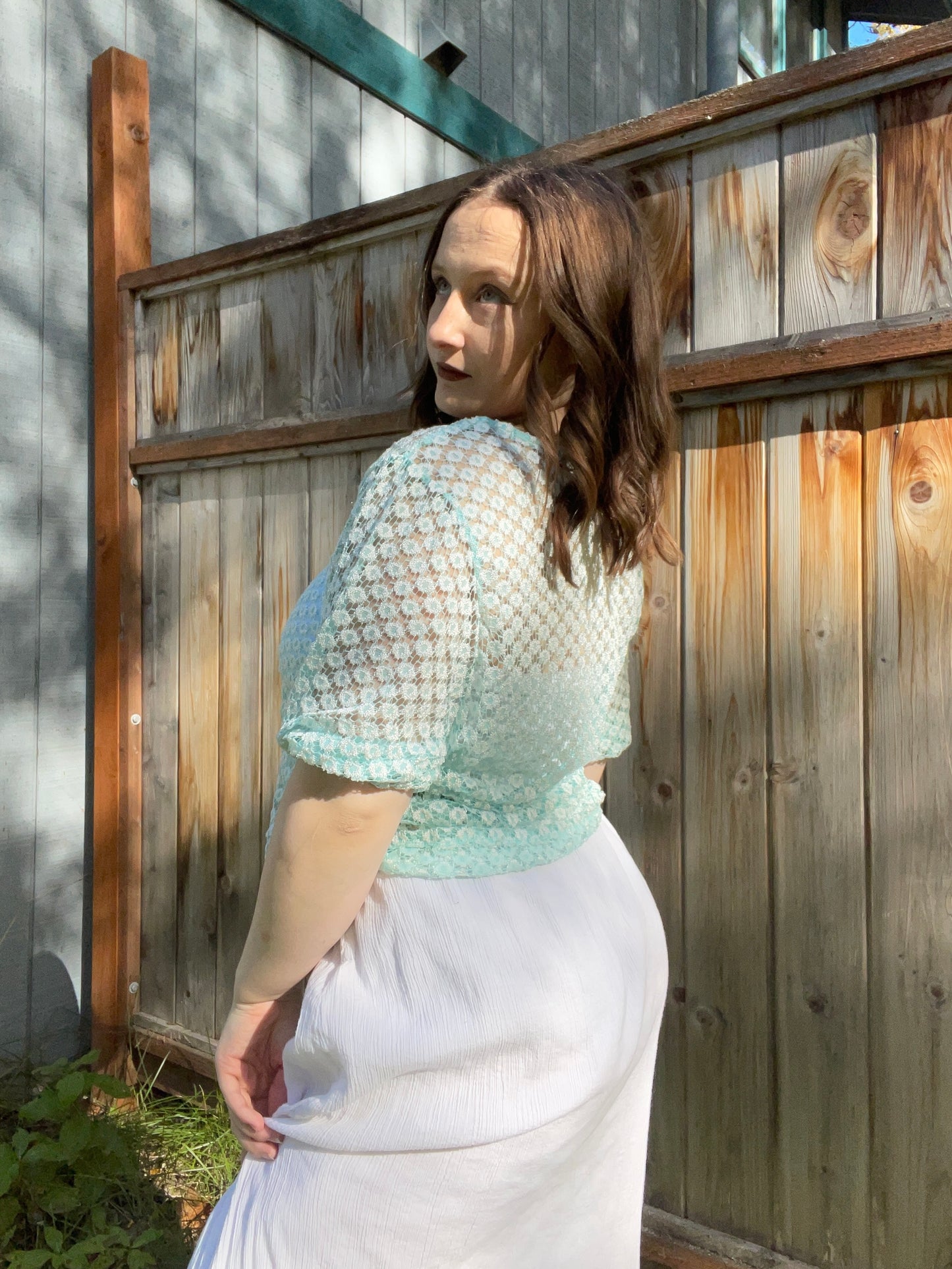 Woman wearing a light blue and white patterned top outdoors against a wooden fence | Grace Thrifts