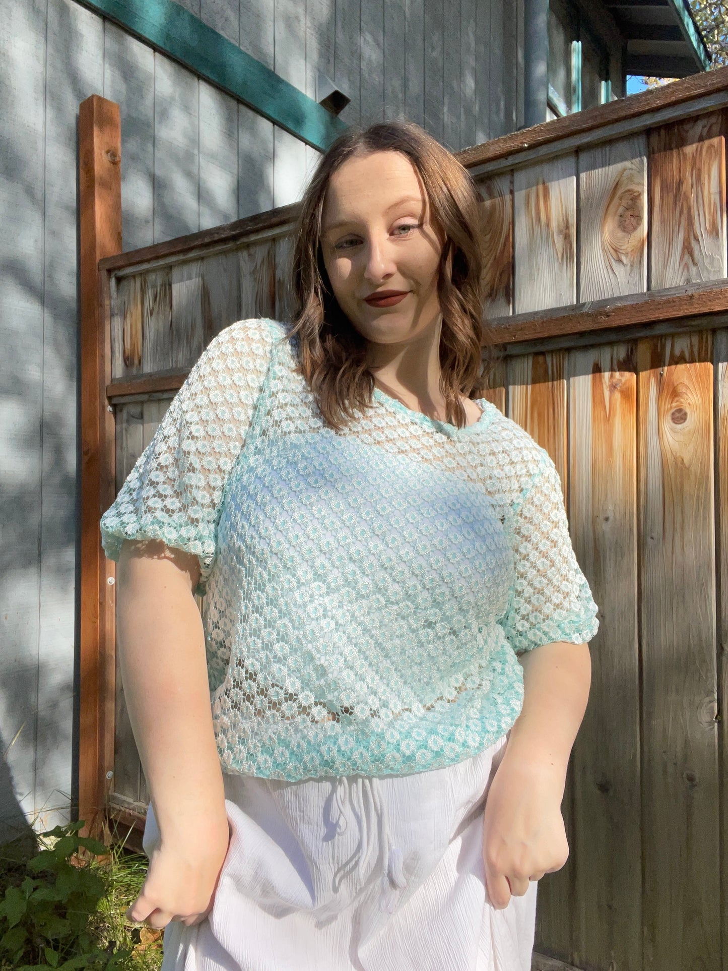 Woman wearing a light blue and white patterned top outdoors against a wooden fence | Grace Thrifts