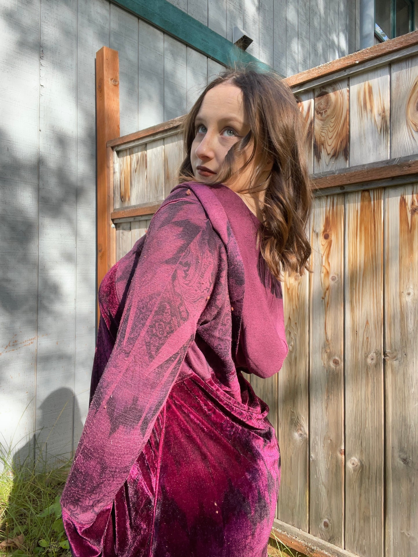 Woman wearing a maroon velvet jacket standing in front of a wooden fence | Grace Thrifts