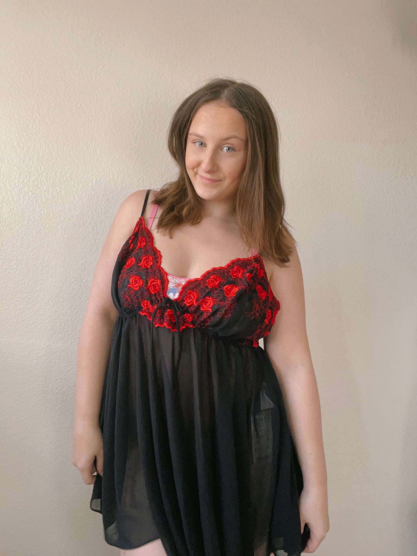 Woman wearing a black dress with red floral lace details against a plain background