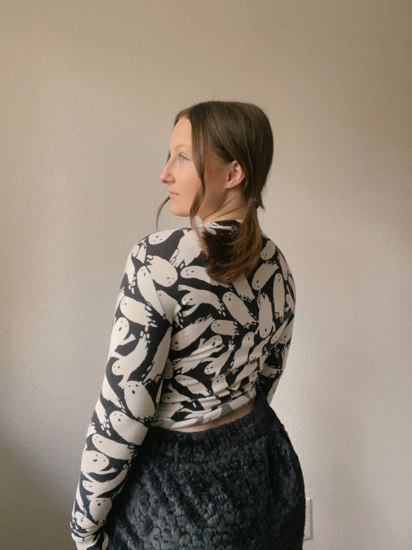 Person wearing a patterned long-sleeve top and dark pants against a plain background
