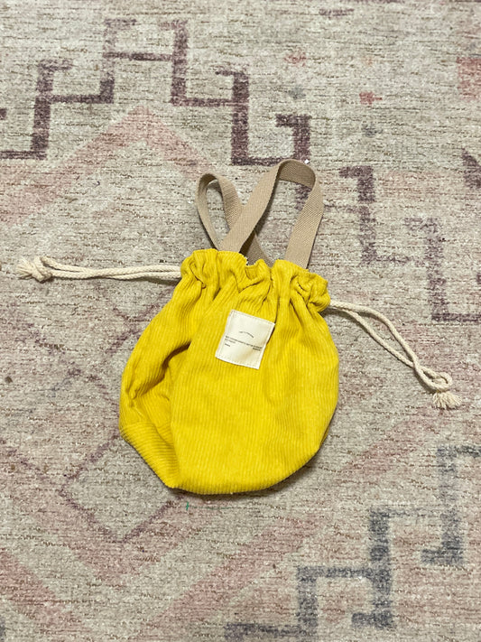 Yellow drawstring bag with a beige strap on a textured surface Yellow Ribbed Drawstring Bag | From the Rack | Grace Thrifts