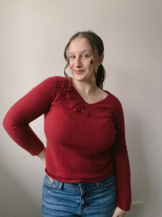 Person wearing a red sweater with floral details and blue jeans against a plain background Cashmere Floral Top | From the Rack | Grace Thrifts