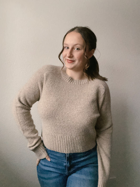 Woman wearing a beige sweater and blue jeans against a plain background Beige Knit Sweater | From the Rack | Grace Thrifts