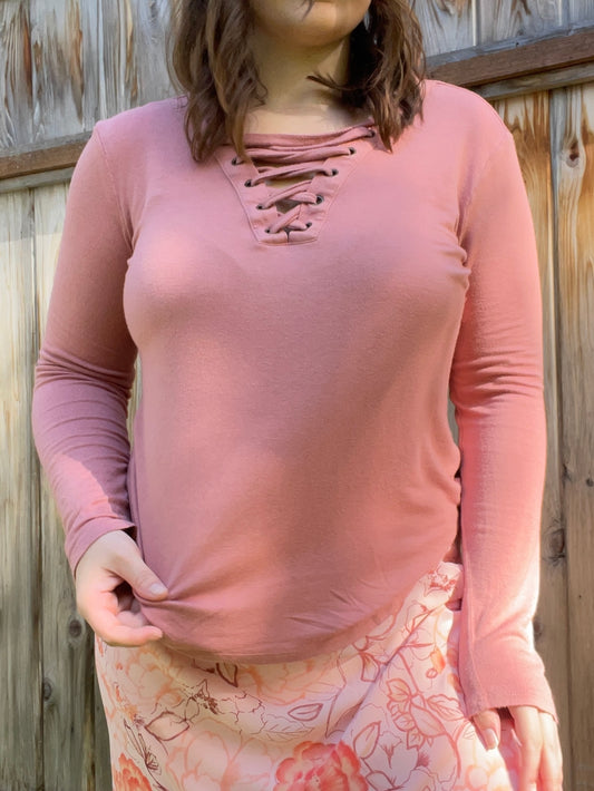 Woman wearing a pink long-sleeve top with lace-up details and a floral skirt standing in front of a wooden fence | Grace Thrifts