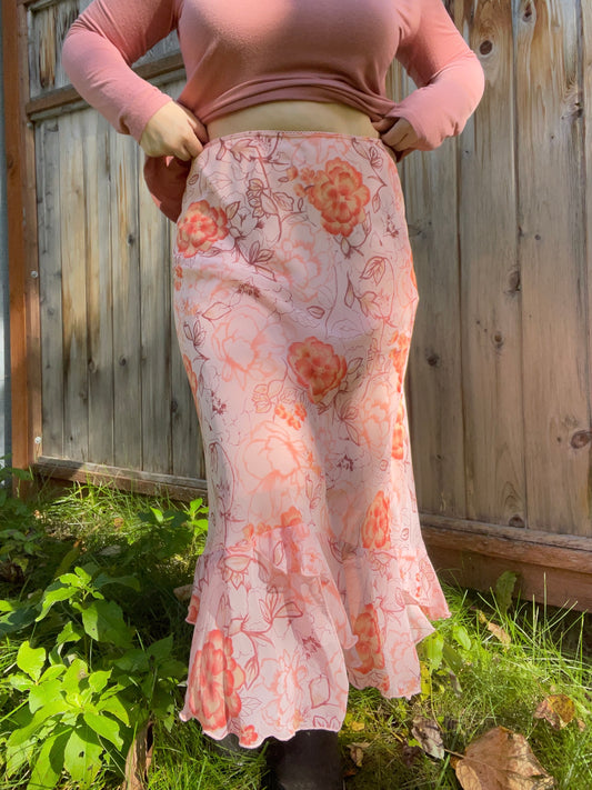 Person wearing a floral skirt with a wooden fence and greenery in the background | Grace Thrifts