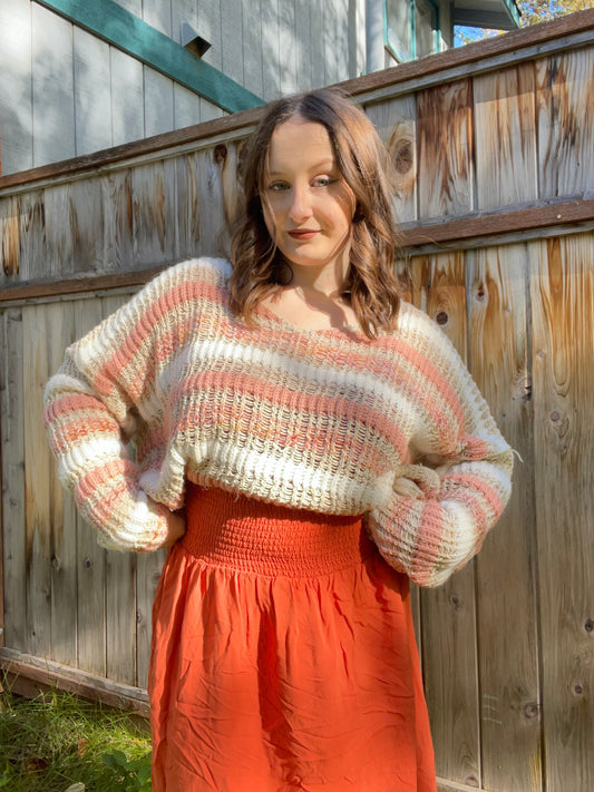 Woman wearing a striped sweater and orange pants standing against a wooden fence | Grace Thrifts