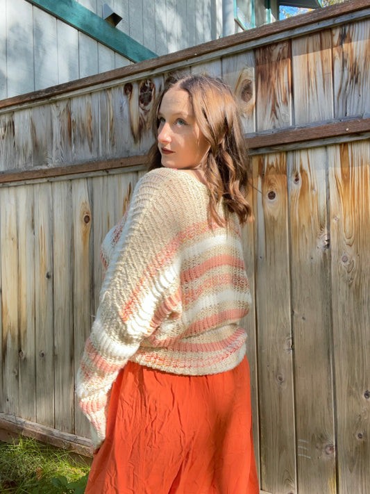 Woman wearing a striped sweater and orange pants standing against a wooden fence | Grace Thrifts