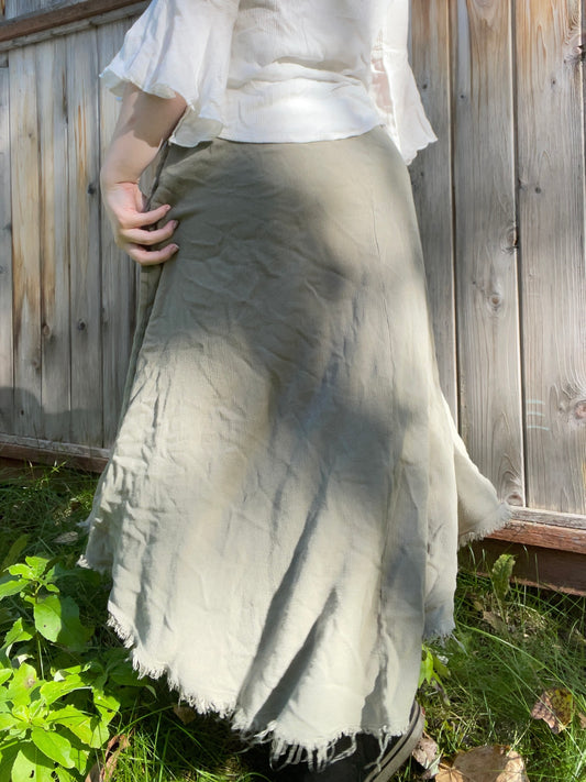 Person wearing a light-colored skirt and white top against a wooden fence background