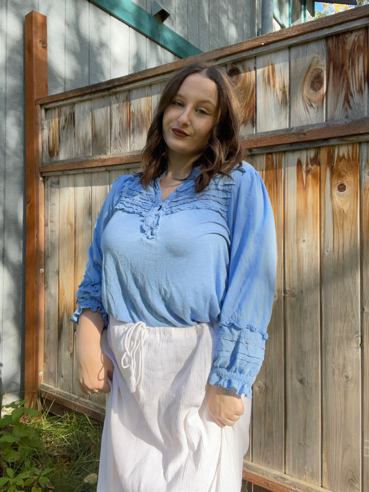 Person wearing a blue blouse with ruffled details in an outdoor setting | Grace Thrifts