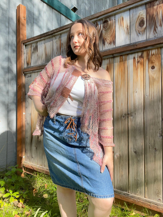 Woman wearing a pink shawl, white top, and denim skirt standing against a wooden fence | Grace Thrifts