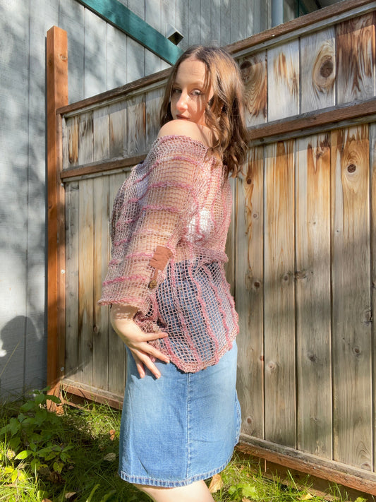 Woman wearing a pink shawl, white top, and denim skirt standing against a wooden fence | Grace Thrifts
