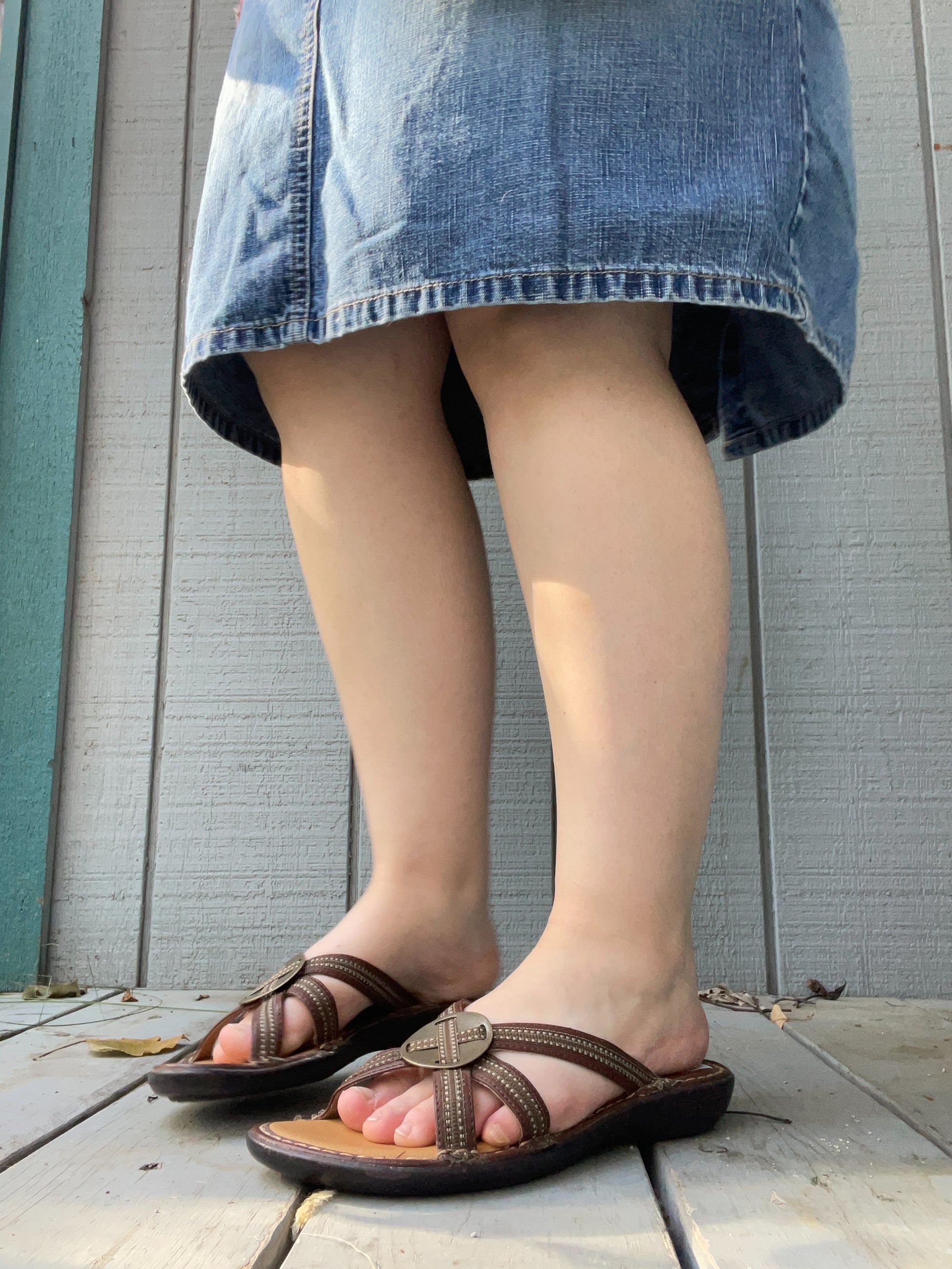 Person wearing brown sandals and a denim skirt on a wooden floor.