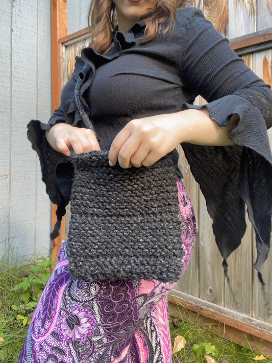 Person holding a gray knitted bag outdoors
