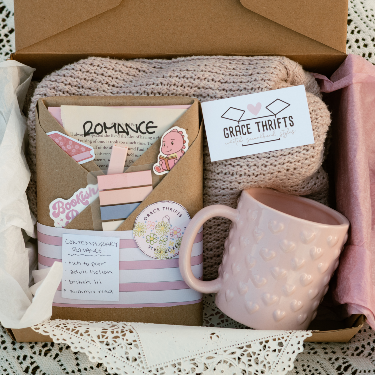 Box containing a pink mug, book, and other items with 'Grace Thrifts' branding.