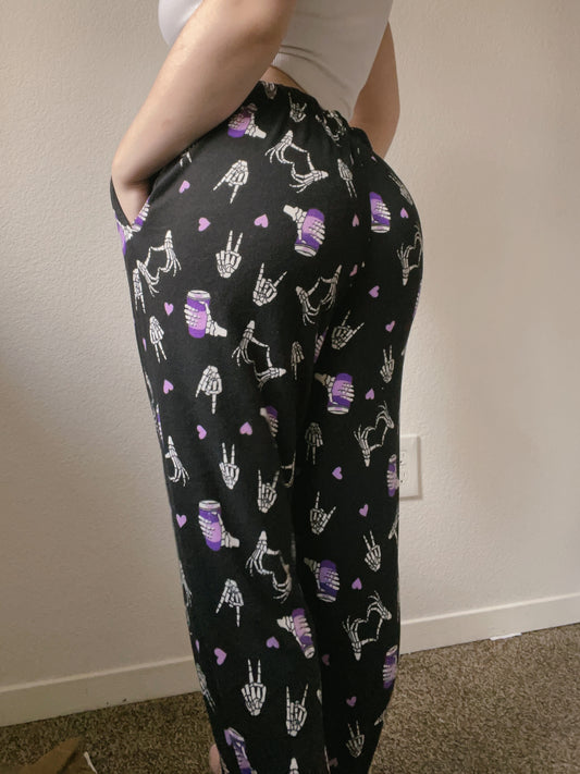 Person wearing black pants with white and purple patterns against a plain wall.