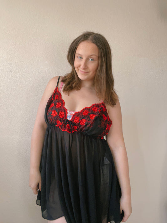 Woman wearing a black dress with red floral lace details against a plain background