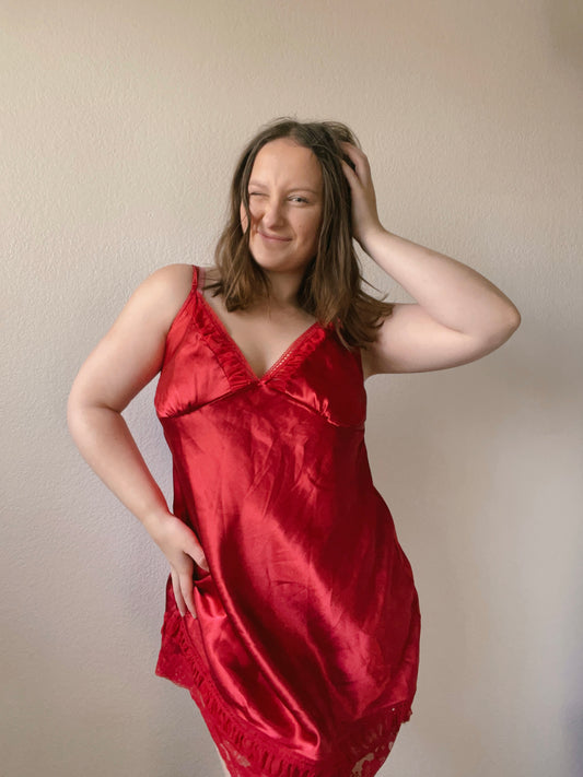 Woman wearing a red satin slip dress against a plain background