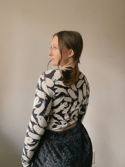 Person wearing a patterned long-sleeve top and dark pants against a plain background