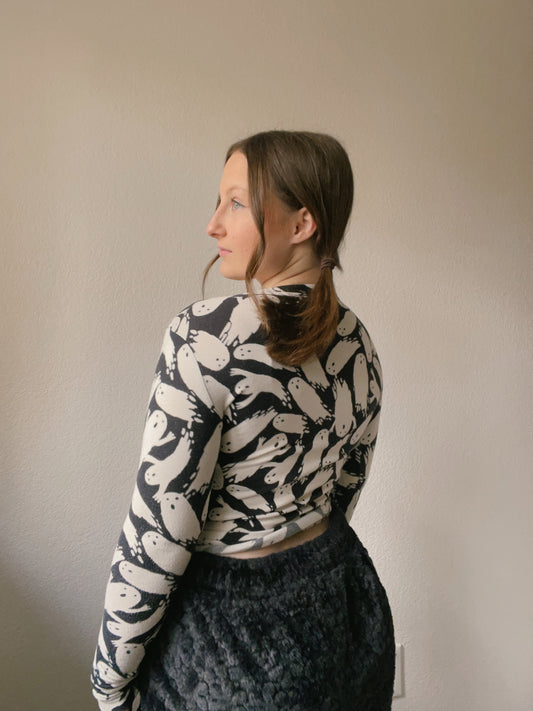 Person wearing a patterned long-sleeve top and dark pants against a plain background